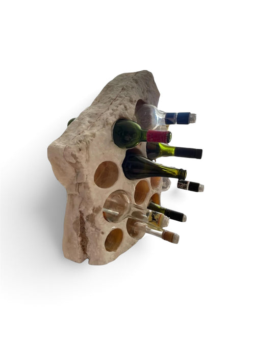 Botellero de piedra natural rústica con nueve cavidades para botellas de vino, visto en ángulo sobre fondo blanco
