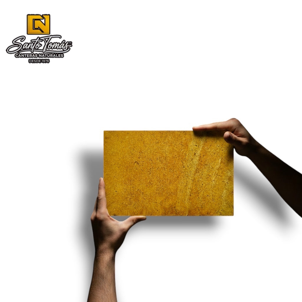 Hands holding a rectangular Canteras Naturales Santo Tomás Cantera Amarilla Calmek stone tile with warm yellow tones.