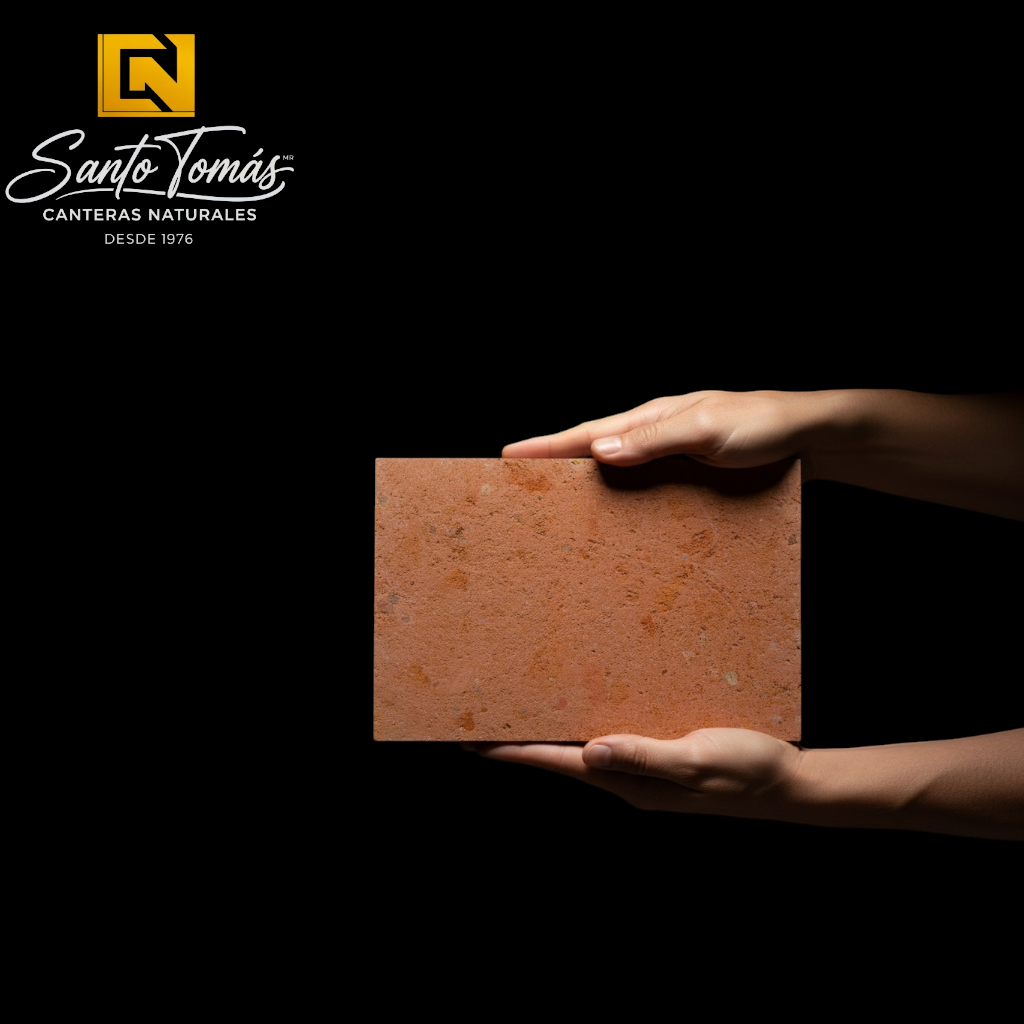 Hands holding a Canteras Naturales Santo Tomás Cantera Roja Tagui stone tile with a fine-grained terracotta texture.