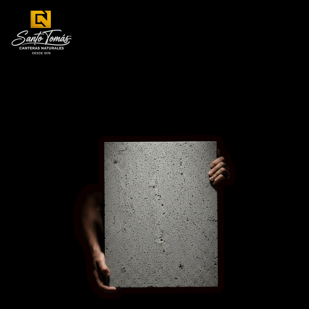 Person holding a rectangular piece of grey Canteras Naturales Santo Tomás volcanic basalt stone with a porous texture.