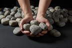 Manos sosteniendo piedra bola gris decorativa para paisajismo, mostrando su textura natural y tamaño a escala.