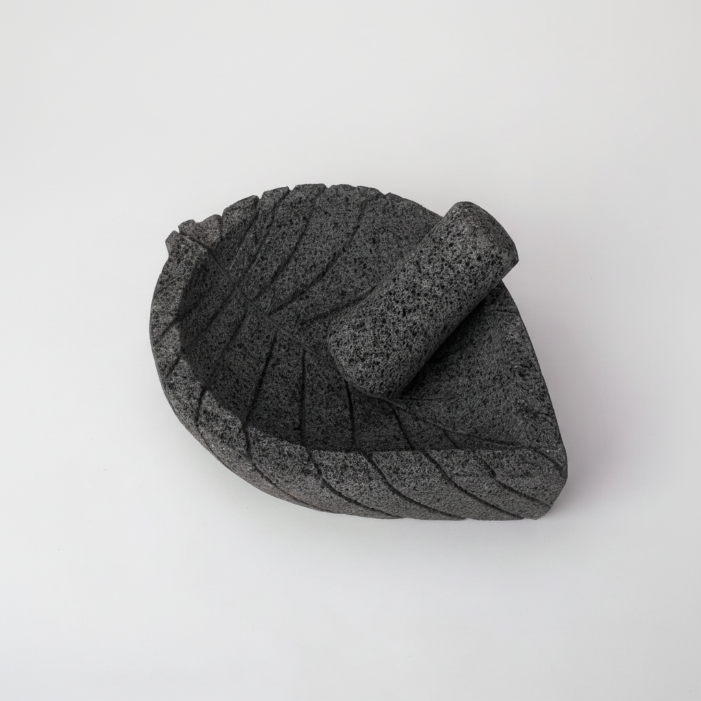 Molcajete tradicional de piedra volcánica basalto con forma de hoja y venas talladas, vista frontal tres cuartos mostrando textura porosa natural