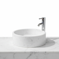 Lavabo ovalín redondo artesanal de mármol Blanco Bego natural de 40 cm con grifo cromado sobre encimera.