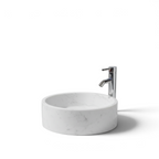 Lavabo ovalín redondo artesanal de mármol Blanco Bego natural de 40 cm con grifo cromado sobre encimera.